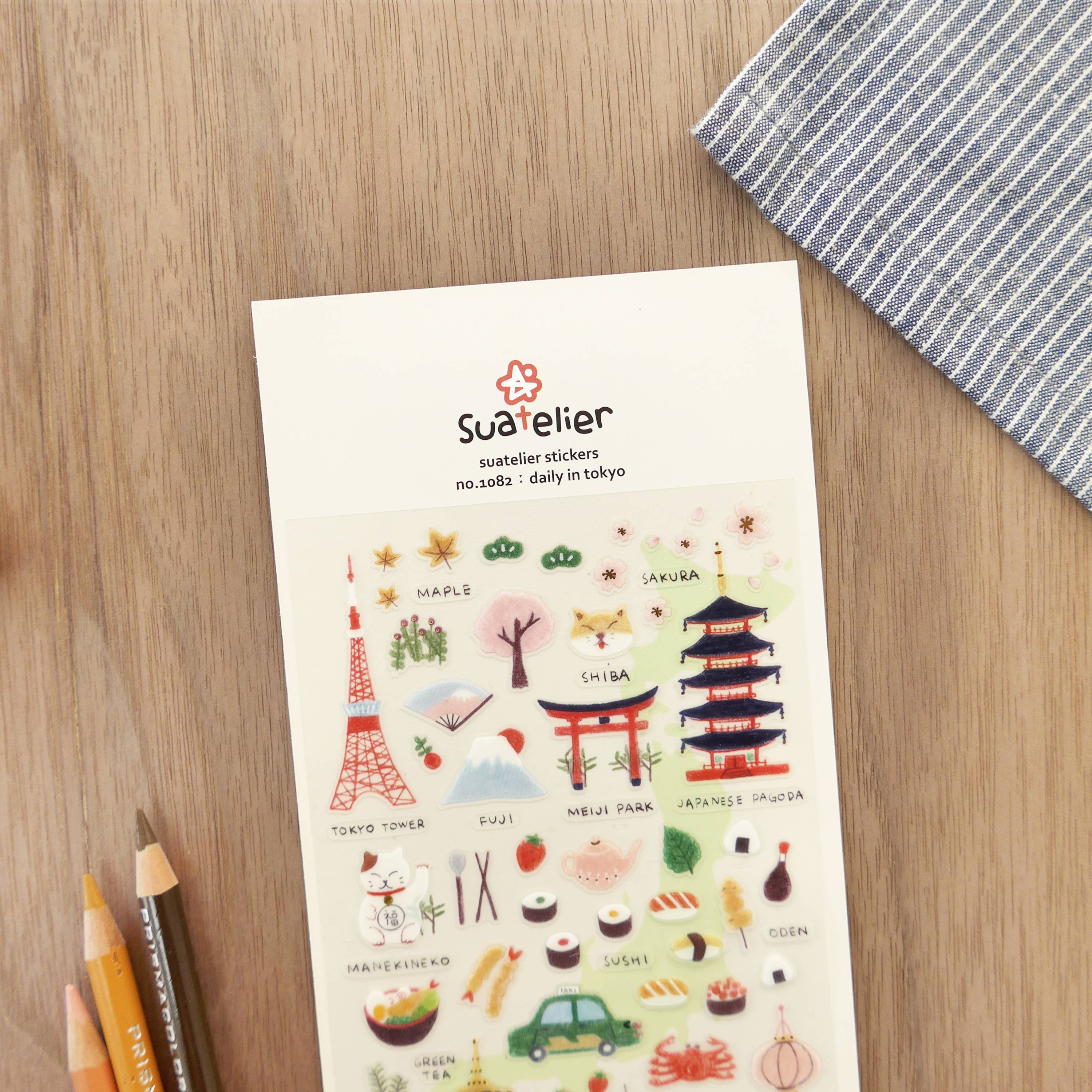 Sheet of stickers with various illustrations on a wooden surface with pencils and a cloth.